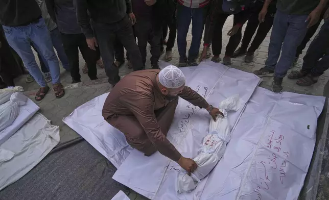A morgue worker places the body of a child among the bodies of other victims killed in at least two separate Israeli army strikes, ahead of a burial ceremony outside Al-Shifa hospital in Gaza City, Monday, May 5, 2025. (AP Photo/Jehad Alshrafi)
