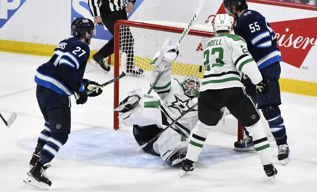 Dallas Stars goaltender Jake Oettinger (29) makes a save as Winnipeg Jets' Mark Scheifele (55) looks for the bouncing puck during second period NHL playoff hockey action in Winnipeg, Thursday, May 15, 2025. (Fred Greenslade/The Canadian Press via AP)