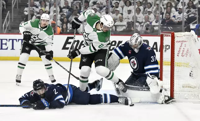 Winnipeg Jets goaltender Connor Hellebuyck (37) makes a save on Dallas Stars' Mason Marchment (27) as Dylan Demelo (2) defends during first period NHL playoff hockey action in Winnipeg, Thursday, May 15, 2025. (Fred Greenslade/The Canadian Press via AP)