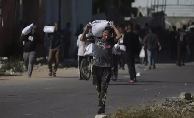 Palestinians carry bags of flour after storming a U.N. World Food Program warehouse in Zawaida, Central Gaza Strip, on Wednesday, May 28, 2025. (AP Photo/Abdel Kareem Hana)