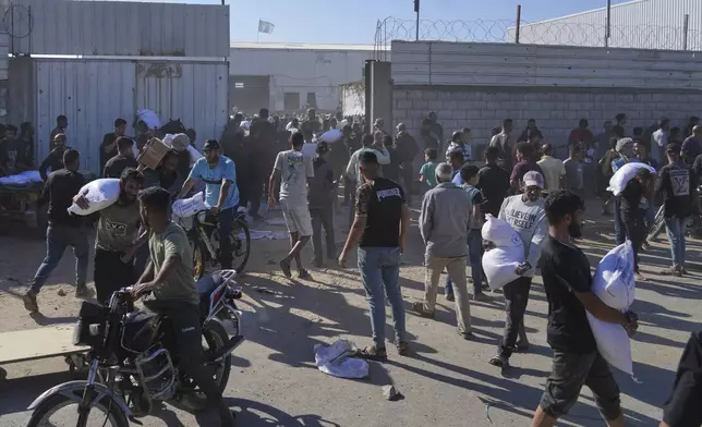 Palestinians carry bags of flour after storming a U.N. World Food Program warehouse in Zawaida, Central Gaza Strip, on Wednesday, May 28, 2025. (AP Photo/Abdel Kareem Hana)