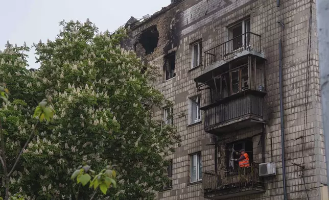 A municipal worker clears the rubble from a balcony of a residential building, damaged after a Russian strike, in Kyiv, Ukraine, on Wednesday, May 7, 2025. (AP Photo/Evgeniy Maloletka)