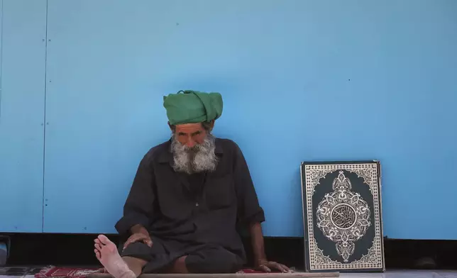 A man sits next to a copy of the Quran at the Sayyida Zeinab Shrine, where many Shiite Muslims believe Zeinab, the granddaughter of Prophet Muhammad, is entombed, in Sayyida Zeinab, south of Damascus, Syria, Saturday, March 15, 2025. (AP Photo/Omar Sanadiki)