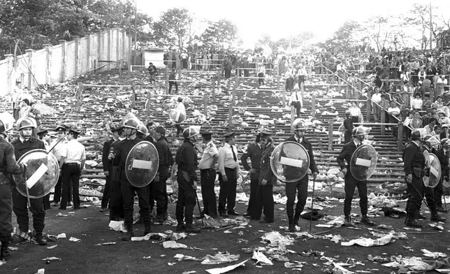 FILE - Belgian riot policemen stand with other police in a line in front of a totally littered stand after various fan groups rioted, in the Heysel Stadium in Brussels, Belgium, Wednesday, May 29, 1985. (AP Photo, File)