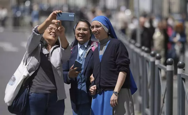 A woman takes selfie with nuns at St. Peter's Square where 133 cardinals are gathering on the second day of the conclave to elect successor of late Pope Francis, at the Vatican, Thursday, May 8, 2025. (AP Photo/Markus Schreiber)