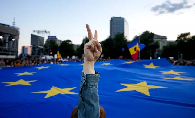 A woman flashes a victory sign backdropped by a European Union flag during an electoral rally of presidential candidate Nicusor Dan, a week ahead of the second round of the country's presidential election redo in Bucharest, Romania, Sunday, May 11, 2025. (AP Photo/Andreea Alexandru)