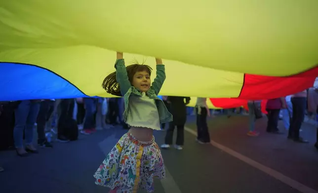 A girl plays underneath a giant national flag during an electoral rally supporting Presidential candidate Nicusor Dan a week ahead of the second round of the country's presidential election redo in Bucharest, Romania, Sunday, May 11, 2025. (AP Photo/Vadim Ghirda)