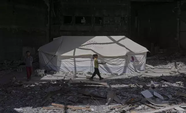 A child carries a tray of food past a tent sheltering displaced Palestinians inside the destroyed Rashad Al-Shawa Cultural Center in Gaza City, Monday, April 21, 2025. (AP Photo/Jehad Alshrafi)