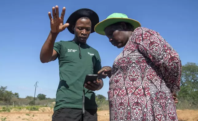 Capon Sibanda, left, a community guardian for encounters between people and elephants, talks with Senzeni Sibanda, a local councilor and farmer, in Hwange, Zimbabwe, Wednesday, April 30, 2025. (AP Photo/Aaron Ufumeli)