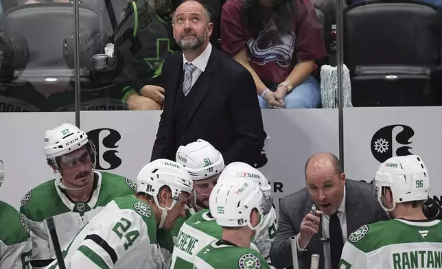 Dallas Stars head coach Peter DeBoer, back, looks at the overhead scoreboard as assistant coach Steve Spott confers with players during a time out in the third period of Game 6 of an NHL first-round hockey playoff series against the Colorado Avalanche Thursday, May 1, 2025, in Denver. (AP Photo/David Zalubowski)