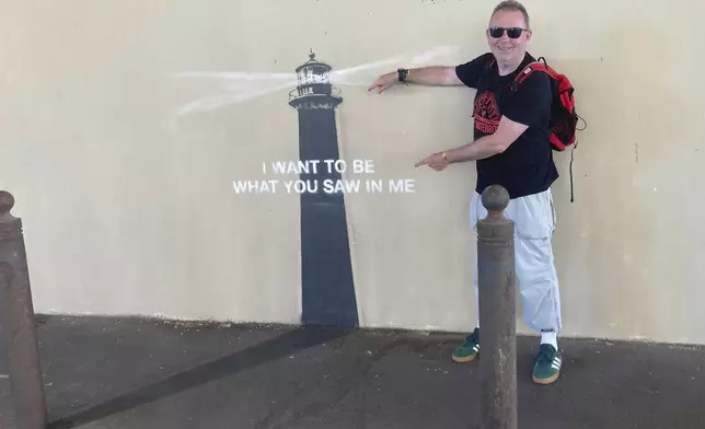 A man poses by an artwork by street artist Banksy, Friday, May 30, 2025 in Marseille, southern France. (AP Photo/Bishr Eltoni)