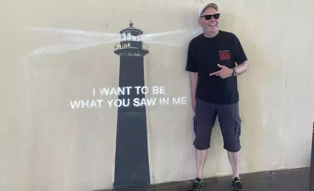 A man poses by an artwork by street artist Banksy, Friday, May 30, 2025 in Marseille, southern France. (AP Photo/Bishr Eltoni)