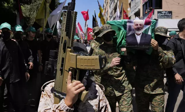 FILE - A boy holds a toy machine gun, as Hamas fighters, right, carry a mock coffin of Hamas political chief Ismail Haniyeh who was killed in an assassination in Tehran, during a symbolic funeral in Beirut, Lebanon, Friday, Aug. 2, 2024. (AP Photo/Hussein Malla, File)