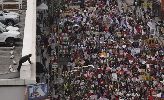 A man leans over the edge of a parking structure to watch demonstrators march during a May Day protest Thursday, May 1, 2025, in Los Angeles. (AP Photo/Jae C. Hong)