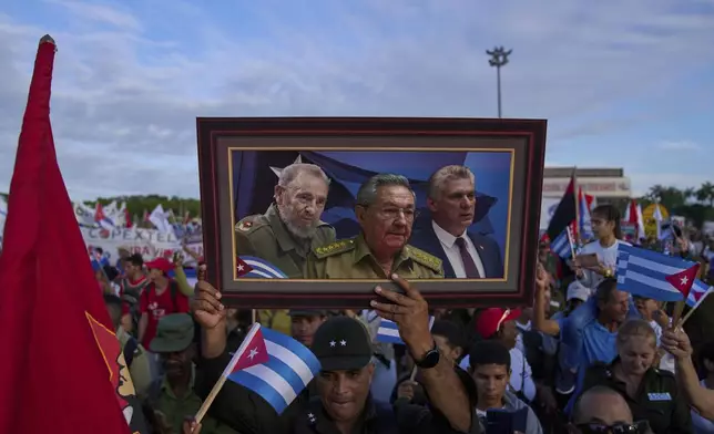 A marcher holds a framed composite image of Fidel Castro, Raul Castro and Cuba's President Miguel Diaz-Canel, during the May Day parade at Revolution Square in Havana, Thursday, May 1, 2025. (AP Photo/Ramon Espinosa)