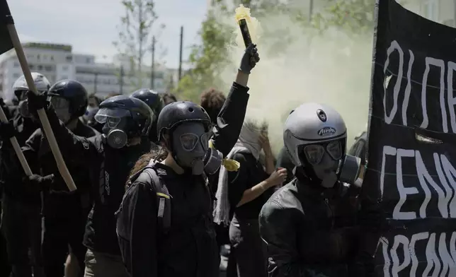 A protester from the anarchist block wearing helmet and tear gas mask, holds a smoke flare during a May Day rally in Athens, Greece, Thursday, May 1, 2025. (AP Photo/Thanassis Stavrakis)