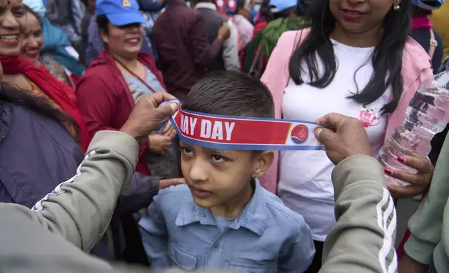 A worker puts a head band on a child's forehead while they get ready to participate in a May Day rally in Kathmandu, Nepal, Thursday, May 1, 2025. (AP Photo/Niranjan Shrestha)