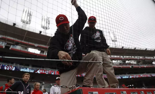 FILE - Members of the grounds crew adjust the new extended netting above the visitors dugout before an opening day baseball game between the Cincinnati Reds and the Washington Nationals, Friday, March 30, 2018, in Cincinnati. (AP Photo/John Minchillo, File)