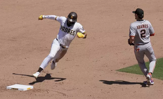 San Diego Padres' Fernando Tatis Jr., left, rounds second base, advancing to third off a single by Luis Arraez as San Francisco Giants shortstop Willy Adames looks on during the fifth inning of a baseball game Wednesday, April 30, 2025, in San Diego. (AP Photo/Gregory Bull)