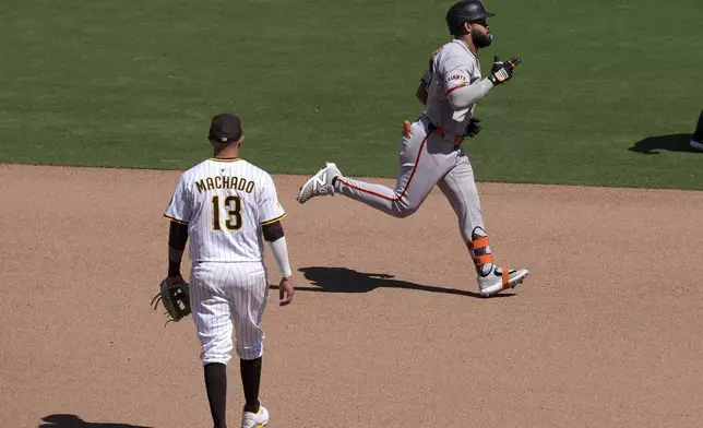 San Francisco Giants' Heliot Ramos, right, passes San Diego Padres third baseman Manny Machado as he rounds the bases after hitting a home run during the seventh inning of a baseball game against the San Diego Padres Wednesday, April 30, 2025, in San Diego. (AP Photo/Gregory Bull)
