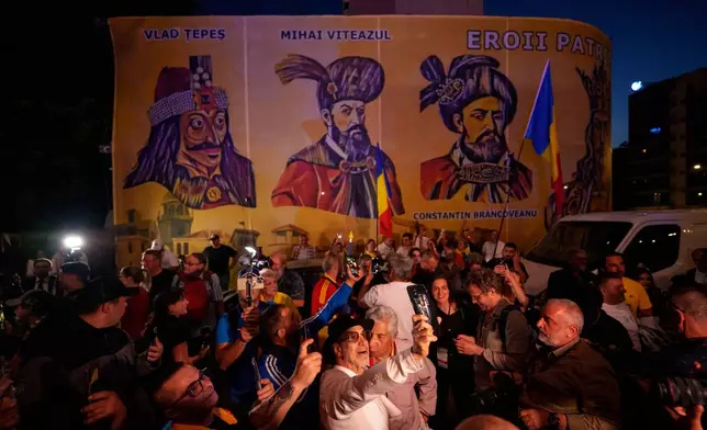 Supporters of presidential candidate George Simion react to the exit poll results, backdropped by depictions of Romanian historical figures, outside the headquarters of the Alliance for the Unity of Romanians (AUR) after polls closed for the first round of the country's presidential election redo in Bucharest, Romania, Sunday, May 4, 2025. (AP Photo/Andreea Alexandru)