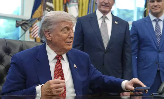 President Donald Trump silences his mobile phone which rang two times as he was speaking to reporters after signing executive orders regarding nuclear energy in the Oval Office of the White House, Friday, May 23, 2025, in Washington. (AP Photo/Evan Vucci)