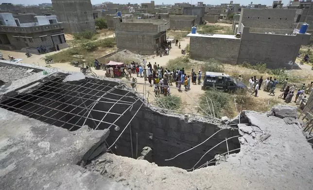 A big hole is seen on a rooftop of a house suspected to have been damaged in Indian drone attack as residents, behind, gather near a cordoned off site, where Pakistan's air defense system shot down a suspected Indian drone in Karachi, Pakistan, Thursday, May 8, 2025. (AP Photo/Fareed Khan)