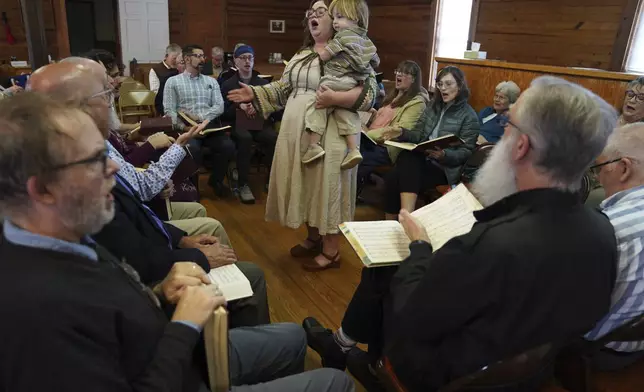 Sarah George, who met her husband through Sacred Harp singing, holds their son while leading a song from the hollow square at a Sacred Harp gathering in Bremen, Ga., at Holly Springs Primitive Baptist Church on Saturday, March 22, 2025. (AP Photo/Jessie Wardarski)