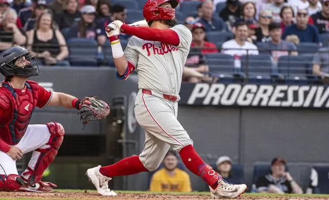Philadelphia Phillies' Kyle Schwarber, right, watches his RBI single off Cleveland Guardians starting pitcher Tanner Bibee as Austin Hedges, left, watches during the fourth inning of a baseball game Saturday, May 10, 2025, in Cleveland. (AP Photo/Phil Long)