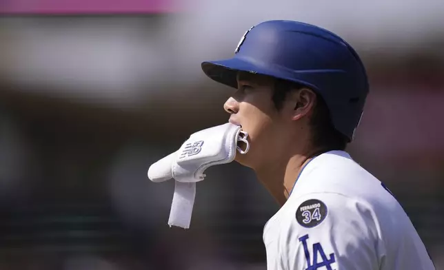 Los Angeles Dodgers' Shohei Ohtani holds his elbow guard in his mouth after hitting a single during the seventh inning of a baseball game against the Los Angeles Angels, Sunday, May 18, 2025, in Los Angeles. (AP Photo/Mark J. Terrill)