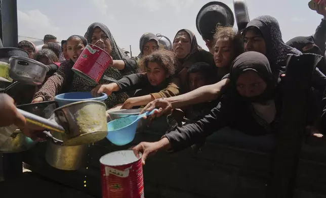 Palestinian children and women struggle to get donated food at a community kitchen in Khan Younis, Gaza Strip, Saturday, May 3, 2025. (AP Photo/Abdel Kareem Hana)