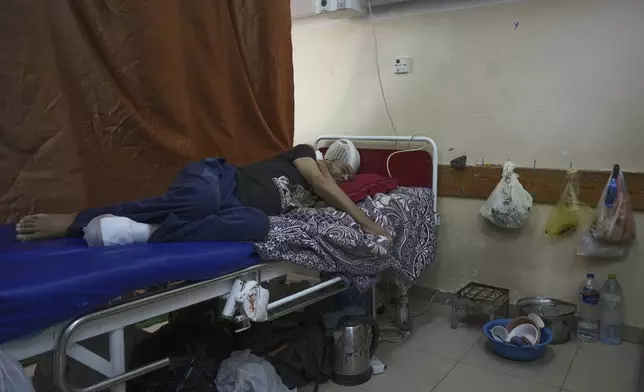 Sobhi al-Bursh, who was injured in a bombing and lost his foot, lies in bed next to dishes and a portable electric stove used to cook food brought from home at Nasser Hospital in Khan Younis, Gaza Strip, Tuesday, May 6, 2025. (AP Photo/Abdel Kareem Hana)