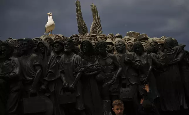 A young boy touches the "Angels Unaware" boat sculpture by Canadian artist Timothy P. Schmalz placed at St. Peter's square at the Vatican, Monday, April 28, 2025. (AP Photo/Francisco Seco)