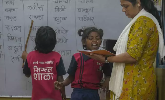 Teacher Sunita Patil checks the notebook of 10-year-old Vaishali Pawar, center, at the Signal Shala school in Thane near Mumbai, India, April 3, 2025. (AP Photo/Rafiq Maqbool)