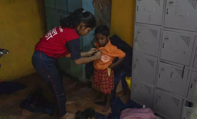 Sonali Goutam Gayakwad, 14, helps a young boy put his uniform on at the Signal Shala school in Thane near Mumbai, India, April 5, 2025. (AP Photo/Rafiq Maqbool)