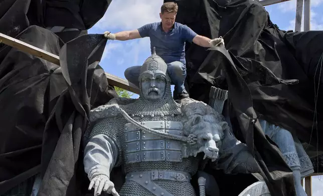 A municipal worker removes the cover that protected a monument to Kyiv legendary founders from Russian missile attacks on the fourth year of Russia-Ukraine war on the country's main square in Kyiv, Ukraine, Wednesday, May 21, 2025. (AP Photo/Efrem Lukatsky)