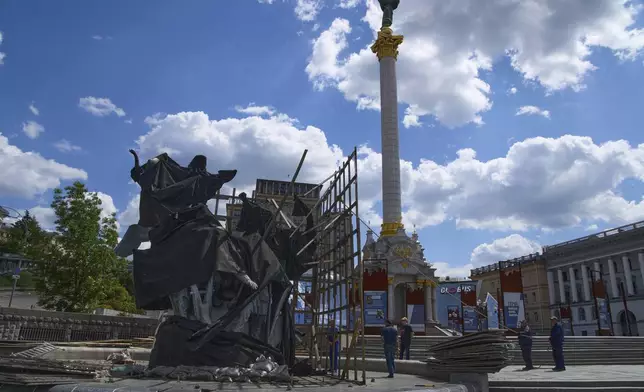 Municipal workers remove the cover that protected a monument of Kyiv legendary founders from Russian missile attacks on the fourth year of Russia-Ukraine war on the country's main square in Kyiv, Ukraine, Wednesday, May 21, 2025. (AP Photo/Efrem Lukatsky)(