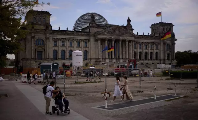 People walk in front of the Reichtag Building, in Berlin, Germany, Friday, May 2, 2025. (AP Photo/Markus Schreiber)