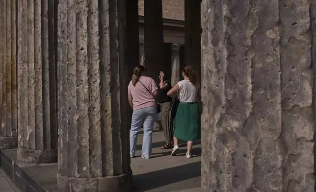 Tourists stand between the columns on Museum Island with holes from artillery fire from World War II, in Berlin, Germany, Friday, May 2, 2025. (AP Photo/Markus Schreiber)
