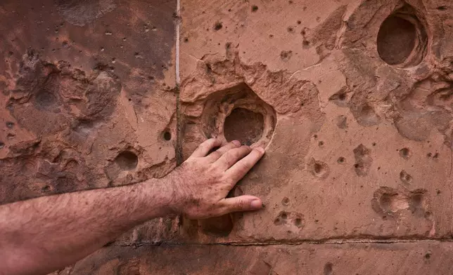 A tourist touches a hole from artillery fire. still visible on the facade of a house eighty years after the end of World War II, in Berlin, Germany, Friday, May 2, 2025. (AP Photo/Markus Schreiber)
