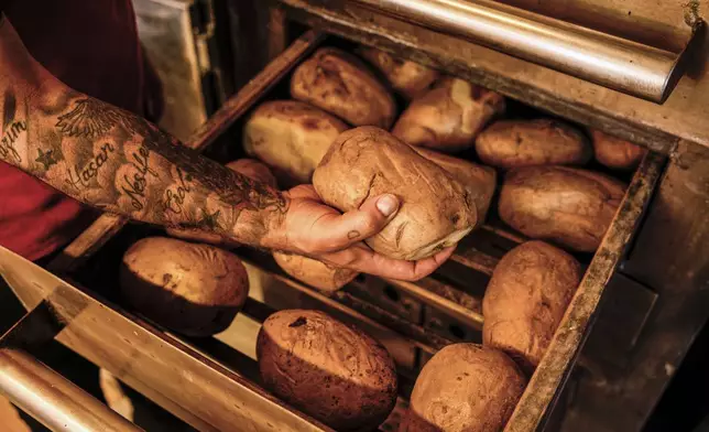 A vendor selects a potato from the oven to prepare the popular Turkish stuffed baked potato dish known as "Kumpir" at Awaterfront square in Ortakoy, Istanbul, Turkey, Friday, May 23, 2025. (AP Photo/Emrah Gurel)