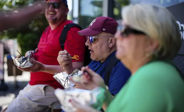 Visitors eat the popular Turkish stuffed baked potato dish known as "Kumpir" at a waterfront square in Ortakoy, Istanbul, Turkey, Friday, May 23, 2025. (AP Photo/Emrah Gurel)