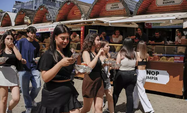 People eat the popular Turkish stuffed baked potato dish known as "Kumpir" while walking at a waterfront square in Ortakoy, Istanbul, Turkey, Friday, May 23, 2025. (AP Photo/Emrah Gurel)
