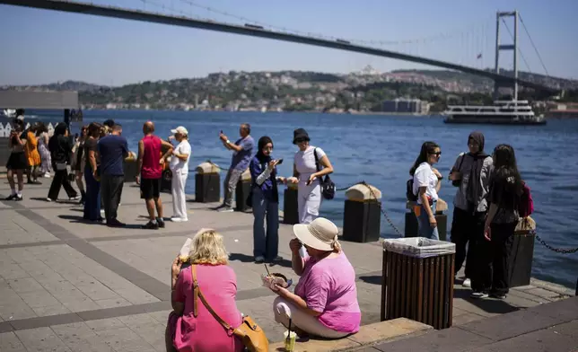 Visitors eat the popular Turkish stuffed baked potato dish known as "Kumpir" at a waterfront square in Ortakoy, Istanbul, Turkey, Friday, May 23, 2025. (AP Photo/Emrah Gurel)
