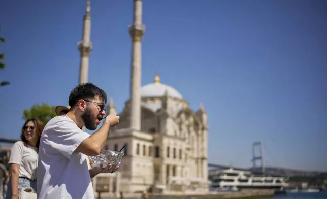 A visitor eats the popular Turkish stuffed baked potato dish known as "Kumpir" at a waterfront square in Ortakoy, Istanbul, Turkey, Friday, May 23, 2025. (AP Photo/Emrah Gurel)