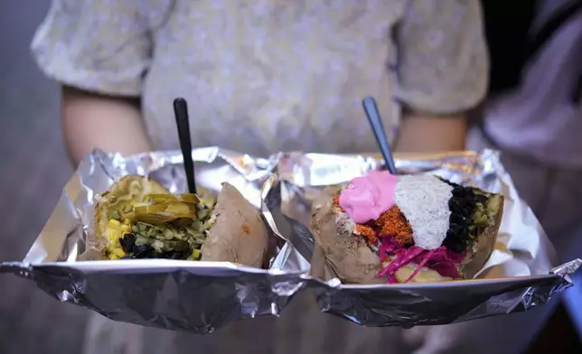 A visitor holds two portions of the popular Turkish stuffed baked potato dish known as "Kumpir" at a waterfront square in Ortakoy, Istanbul, Turkey, Friday, May 23, 2025. (AP Photo/Emrah Gurel)
