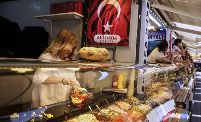 A vendor prepares the popular Turkish stuffed baked potato dish known as "Kumpir" at a waterfront square in Ortakoy, Istanbul, Turkey, Friday, May 23, 2025. (AP Photo/Emrah Gurel)