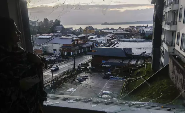 A woman looks through her home's broken window at more damage the day after tornado hit Puerto Varas, Chile, Monday, May 26, 2025. (AP Photo/Patricio Aguayo)