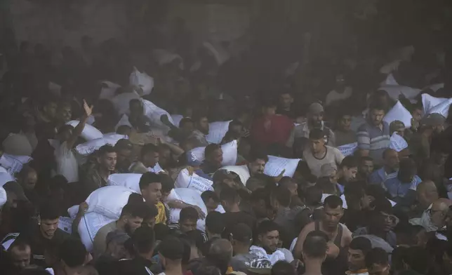Palestinians carry bags of flour after storming a U.N. World Food Program warehouse in Zawaida, Central Gaza Strip, on Wednesday, May 28, 2025. (AP Photo/Abdel Kareem Hana)