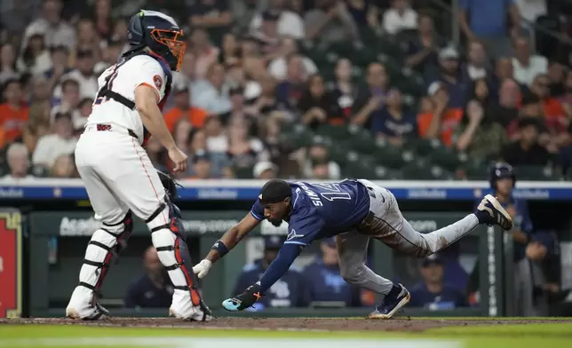 Tampa Bay Rays' Chandler Simpson (14) dives home to score a run on a throwing error by Houston Astros catcher Yainer Diaz (21) as Kameron Misner struck out during the fourth inning of a baseball game, Thursday, May 29, 2025, in Houston. (AP Photo/Karen Warren)